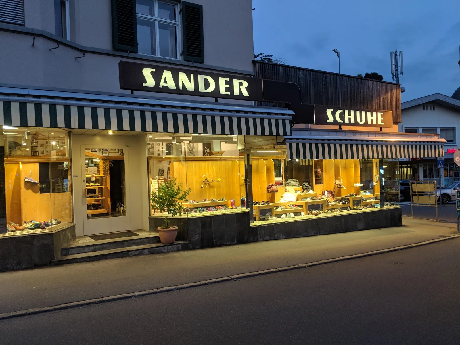 Die beleuchteten Schilder SANDER und SCHUHE über den Schaufenstern des Geschäfts in der Abenddämmerung