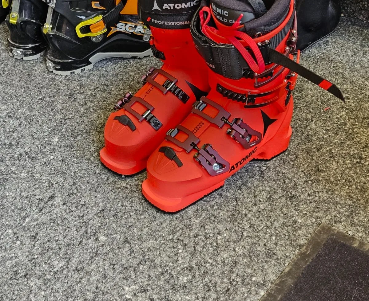 Ein roter Skischuh der Marke Atomic und schwarze Skischuhe der Marke Scarpa stehen auf dem Boden des Geschäfts
