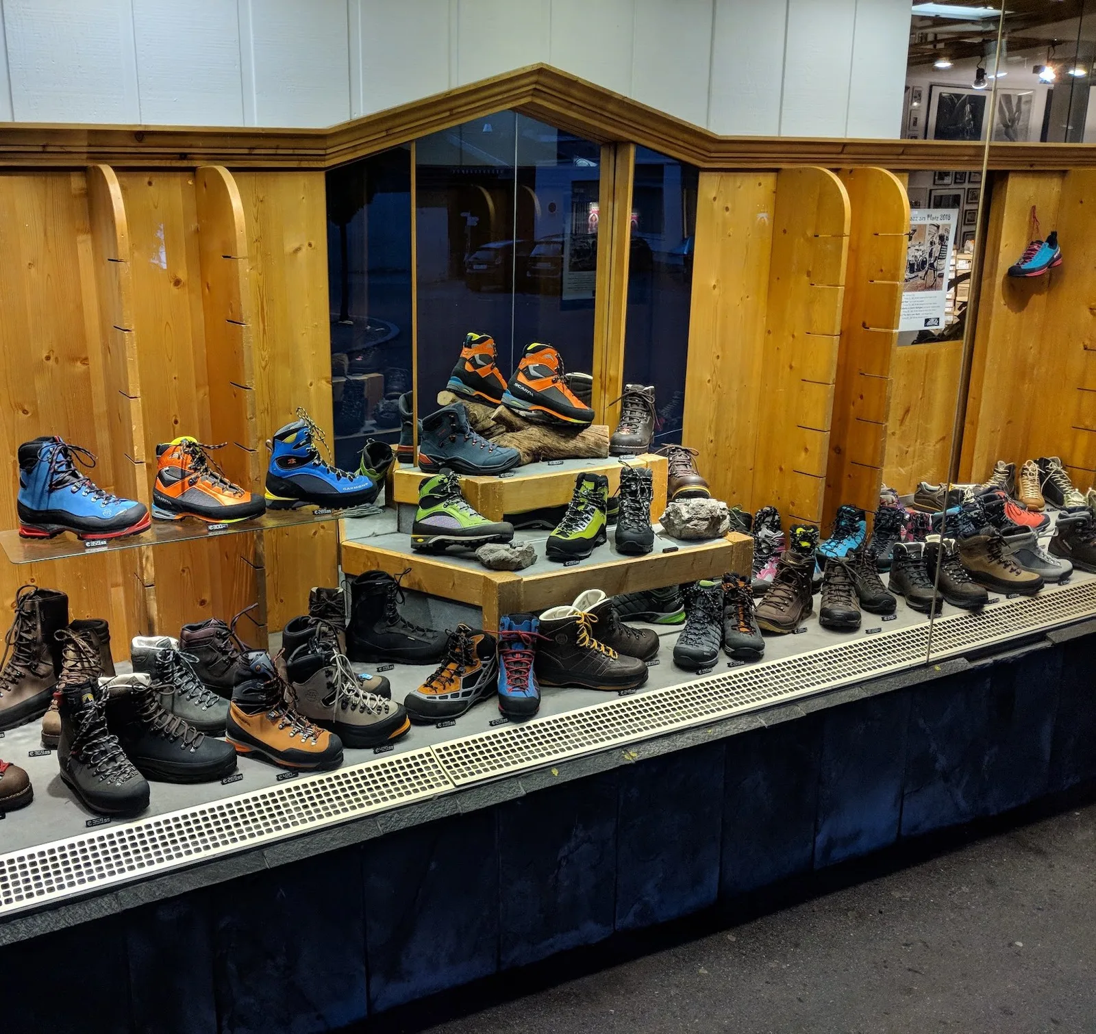 Schaufenster mit Berg- und Wanderschuhen auf Holzstufen und Steinen, dahinter eine Wand aus hellem Fichtenholz