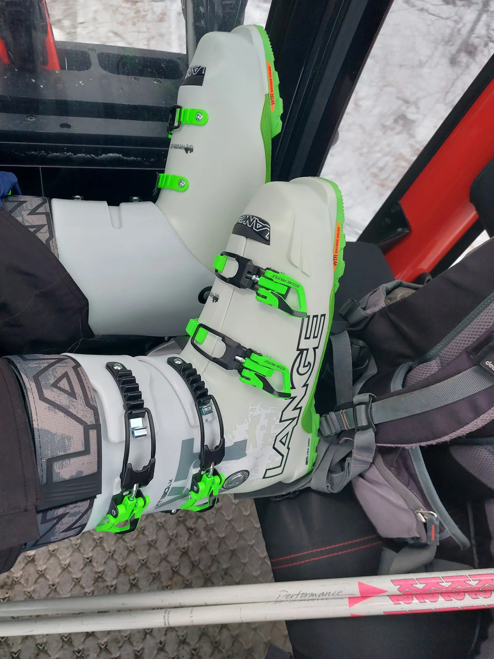 Zwei weiß-grüne Skischuhe der Marke Lange in einem Sessellift, daneben ein Rucksack und ein Paar Ski
